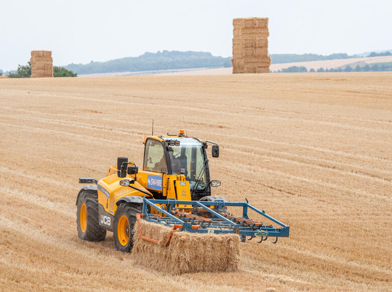 542-70 JCB telehandler with flat eight grab picking up a straw bale in a stubble field