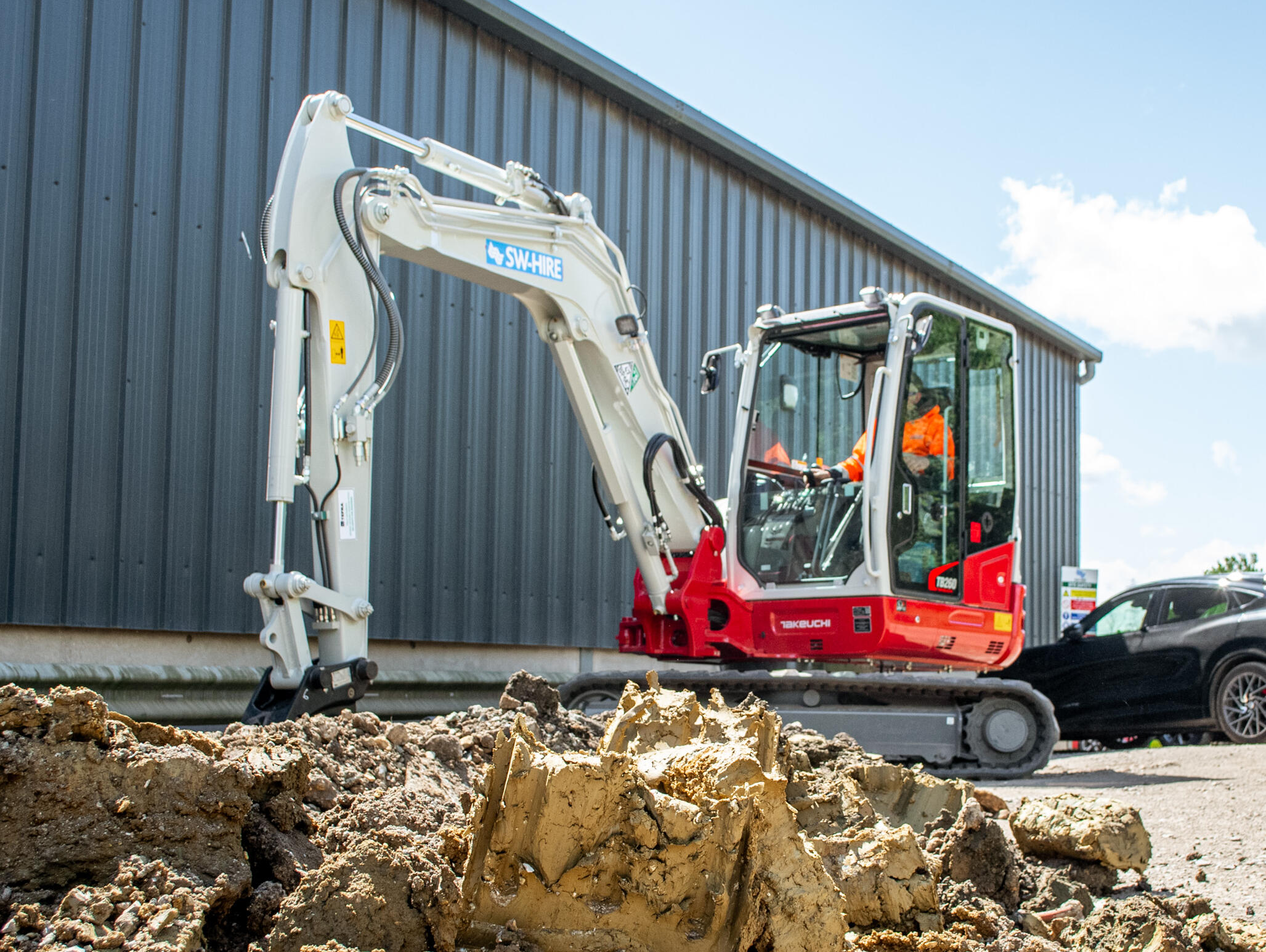 Takeuchi TB260 excavator digging up a channel behind a workshop