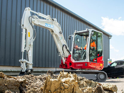 Takeuchi TB260 excavator digging up a channel behind a workshop